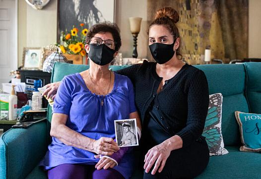 Elvia Sandoval and her daughter, Marcella Reed, pose with a photo of Reed’s grandfather, Walter Anderson, who contracted COVID-1