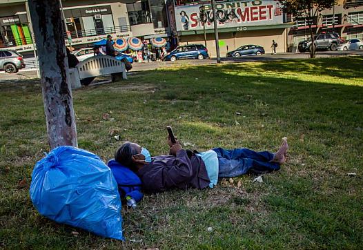 A homeless man lies on the grass in MacArthur Park in Los Angeles in May.