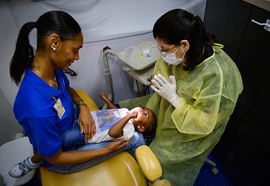 Shatorra Morris holds Kieraney Morris, 2, as Dr. Maria Pardo encourages Kieraney as she brushes her own teeth inside the MCR Hea
