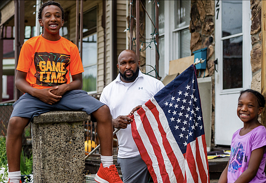 Jaden Weems, left, joins his father James Weems, who was in the process of installing a flag on his home, and Mr. Weems' daughte