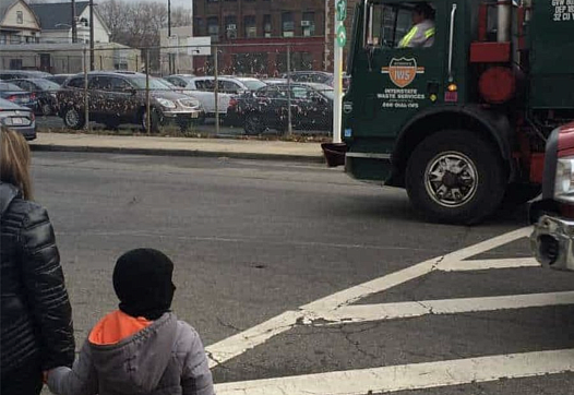 Trucks rumble along the road outside Hawkins Street School in Newark, New Jersey, as a family waits to cross.