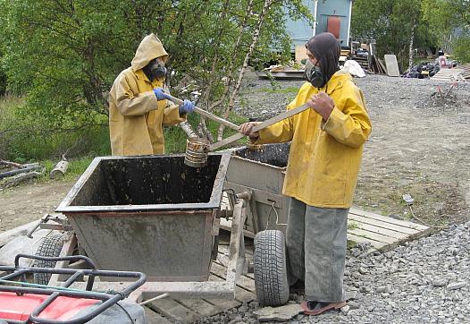 A 2011 photo shows residents of Pitkas Point, Alaska wearing breathing apparatus transfer human waste to a collection bucket, wh
