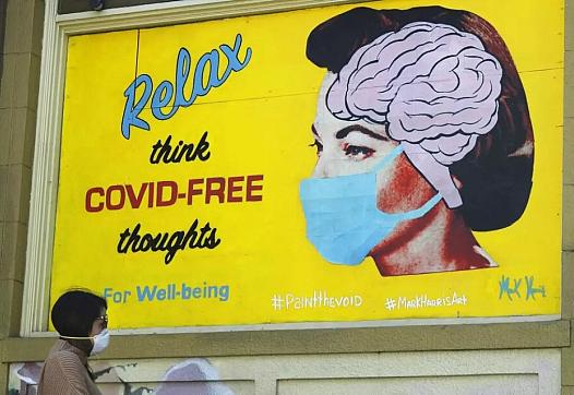 A woman wears a face mask while walking under a sign that reads "Relax think COVID free thoughts" during the coronavirus outbrea