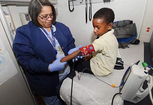 Tanisha Jones checks the blood pressure of Derrick Jenkins, 7, aboard a mobile clinic outside Dixon elementary school. (Photos by Max Ortiz / The Detroit News)  