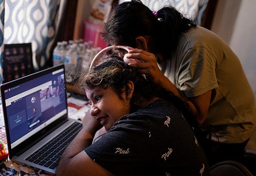 Sarai Camarillo (right) shares headphones with her sister, Isamari Lucero, 13, as she learns remotely from their Little Village