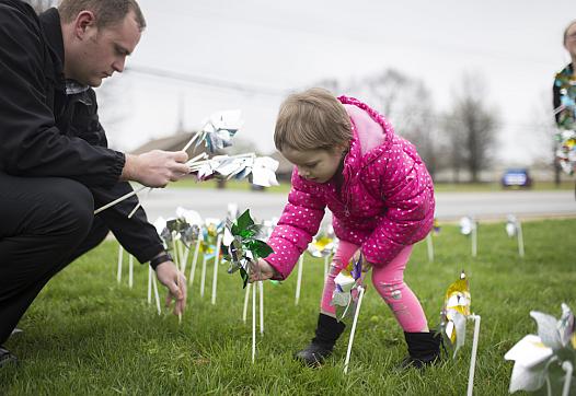 Elizabeth Crouch, 4, (center) places pinwheels in the ground with Det. Adam Corbett