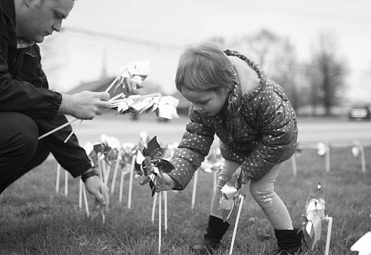 A young girl places pinwheels in the ground with a detective at the Bentonville Police Station at a rally to raise awareness of 