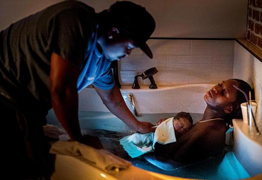 Dennis touches their son as Aysha rests in the birthing bath at Kindred Space LA’s South LA birthing center on Mother’s Day nigh