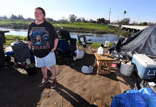 Becky Walthan, 45, stands outside of her tent along the east bank of the Stockton Diverting Canal. 