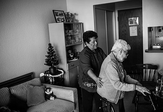 Maria Martínez helps her client, Agripina Castellanos, as she walks inside her Angelus Plaza apartment. (Photo by Bear Guerra)