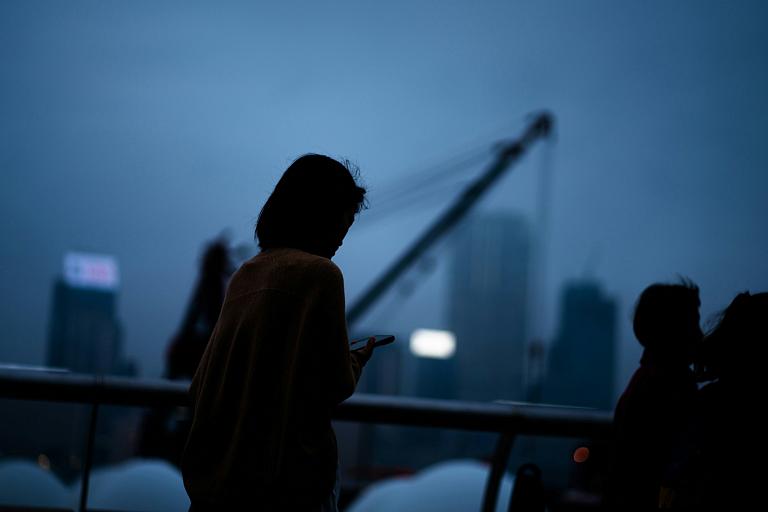 Woman looks at phone amid a dark sky background.