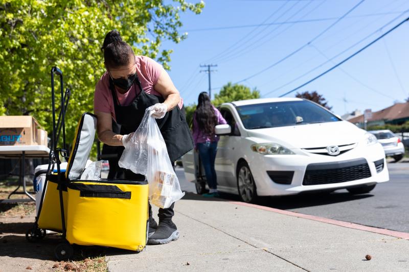 Consuelo Meza fills a bag with milk for a client at a food pick-up site at the Los Robles Ronald McNair Academy in East Palo Alto on April 28, 2021. Photo by Magali Gauthier.