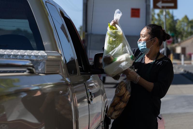 Norma Lazcano places bags of food in a client's car at a food pick-up site at the Los Robles Ronald McNair Academy in East Palo Alto on May 19, 2021. Photo by Magali Gauthier.
