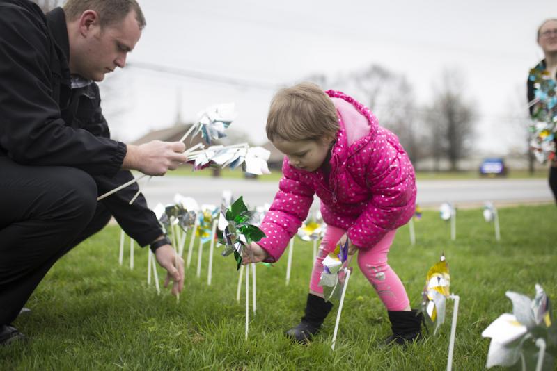 Elizabeth Crouch, 4, (center) places pinwheels in the ground with Det. Adam Corbett (left), at the Bentonville Police Station at a Cherishing Children rally in April 2018 to recognize child abuse investigators and promote prevention of child maltreatment. The pinwheels represented each confirmed case of child abuse and served as a reminder of a child's innocence. Doves released at the rally recognized children who had died of abuse.