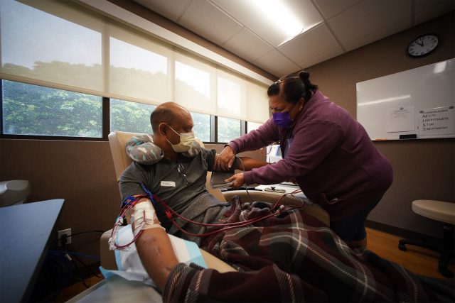 Kim Pagan adjusts her husband’s blood pressure device as he practices on the in-home dialysis machine. 