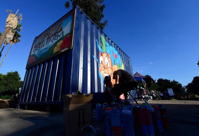 Pomona artist Joeded Walsh paints a mural on the side of the food pantry during the launch of the daily farmers market, Bodega Comunitaria, at the Lopez Urban Farm in Pomona on Wednesday, Aug. 17, 2022. (Photo by Will Lester, Inland Valley Daily Bulletin/SCNG)