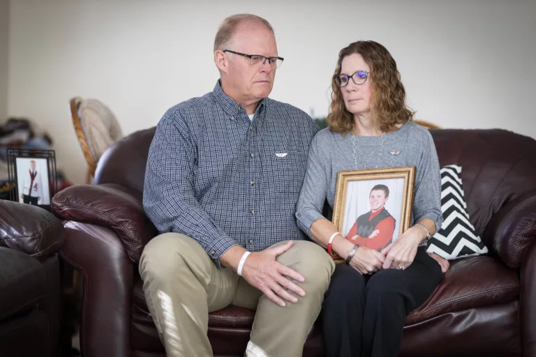 Gary Peters and Shari Peters sit in the living room of their home in Aurora on Saturday, Oct. 22, 2022, while Shari holds a photo of their son Jacob, who died of lymphoma on Nov. 16, 2011, at the age of 17. The Peters have concerns about nitrate in Nebraska’s drinking water and its possible link to pediatric cancers. Gary Peters said it isn’t enough to avoid drinking contaminated water. Bathing and cooking with it should worry Nebraskans, too, he said. Photo by Ryan Soderlin for the Flatwater Free Press