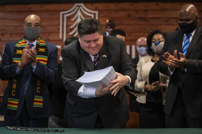 Flanked by lawmakers and supporters, Gov. J.B. Pritzker picks up the more than 700-page criminal justice reform bill after signing it into law during a ceremony at Chicago State University last year.Ashlee Rezin / Sun-Times file