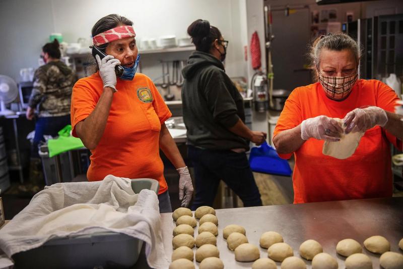 Cam Ogle, left, answers the phone while Lody Kent, right, makes fry bread for senior lunch at the Keller senior meal site. Kent runs the site, which is not wired, unlike most tribal government buildings. Even phone service can be unreliable at the site. (Amanda Snyder / The Seattle Times)